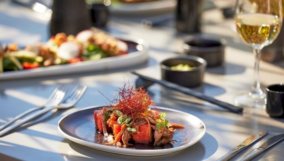 Speisen auf dem Tisch im Hotel Ikos Odisia, einschließlich eines Tellers mit Fleisch und Gemüse und einem Glas Wein.