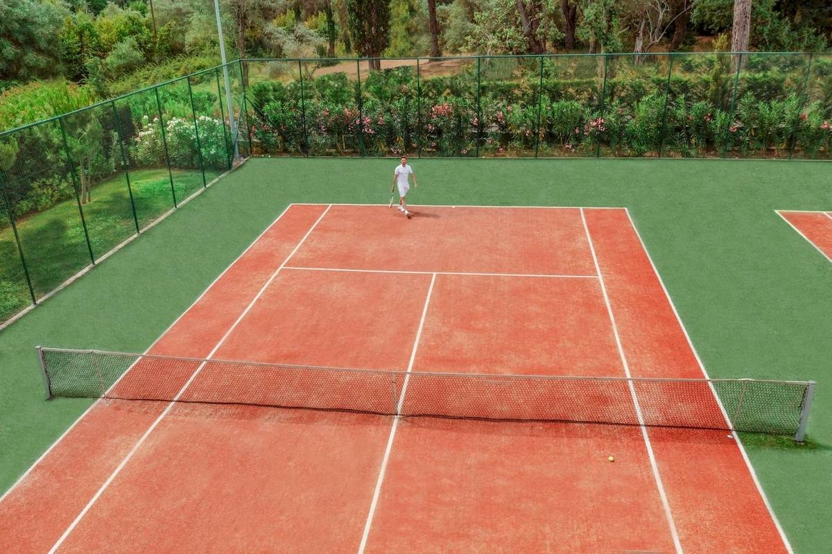 Tennisplatz im Freien im Ikos Odisia Hotel, ein Spieler steht auf dem Platz.
