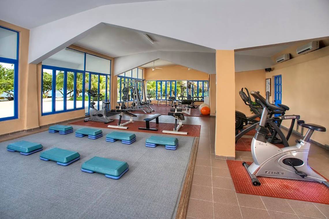 Fitnessstudio im Memories Jibacoa Resort mit verschiedenen Geräten und Fenstern zum Meer.