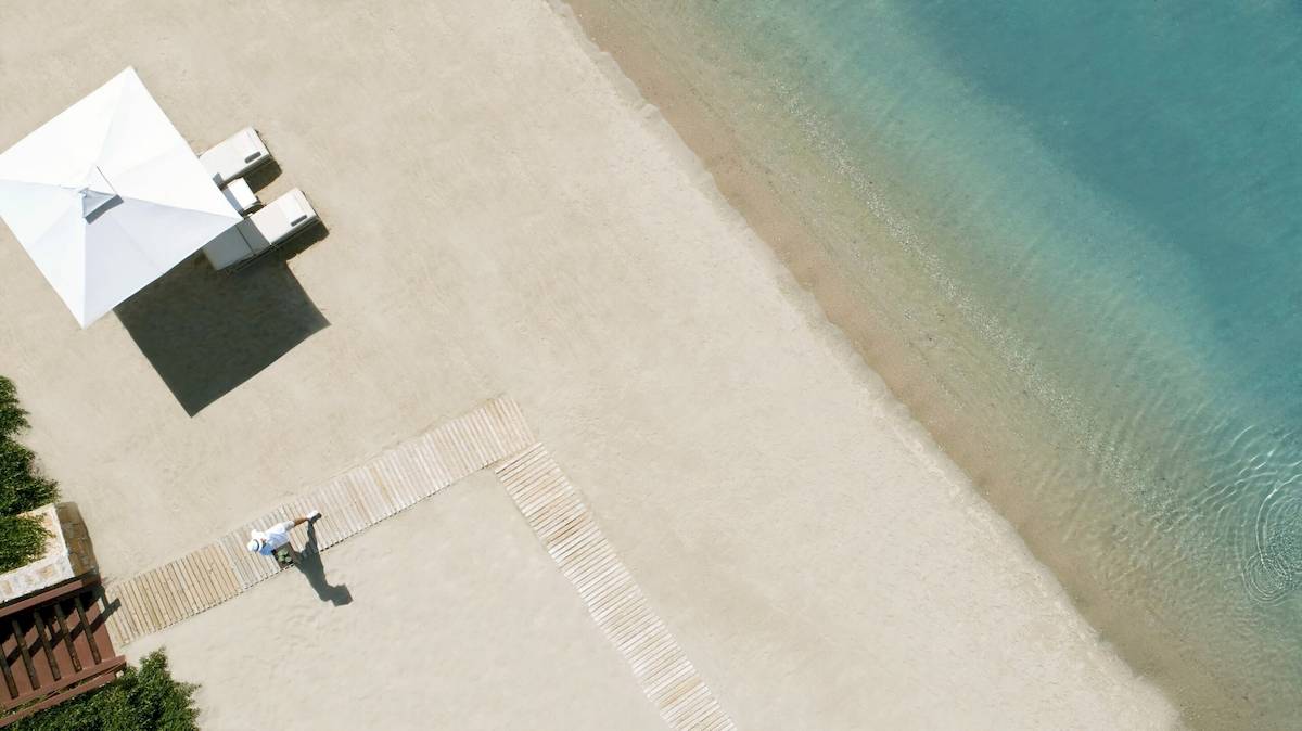 Strandszene mit einem weißen Strandhut und einer Person, die auf dem Ikos Olivia steht.