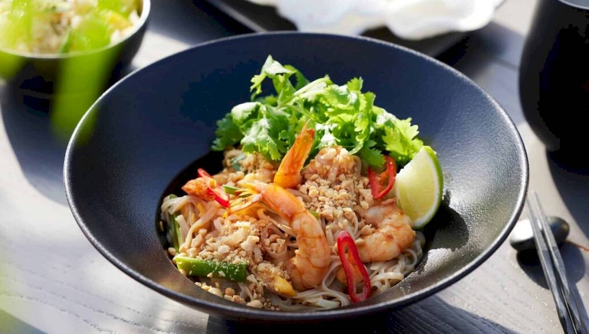 Ein Teller mit Shrimp-Nudel-Gericht in einer schwarzen Schüssel, garniert mit Limettenscheibe und Gemüse.