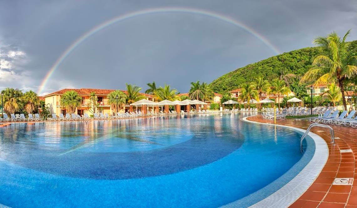 Ein großer Pool mit vielen Sonnenliegen und einem Regenbogen am Himmel, im Memories Jibacoa Resort.