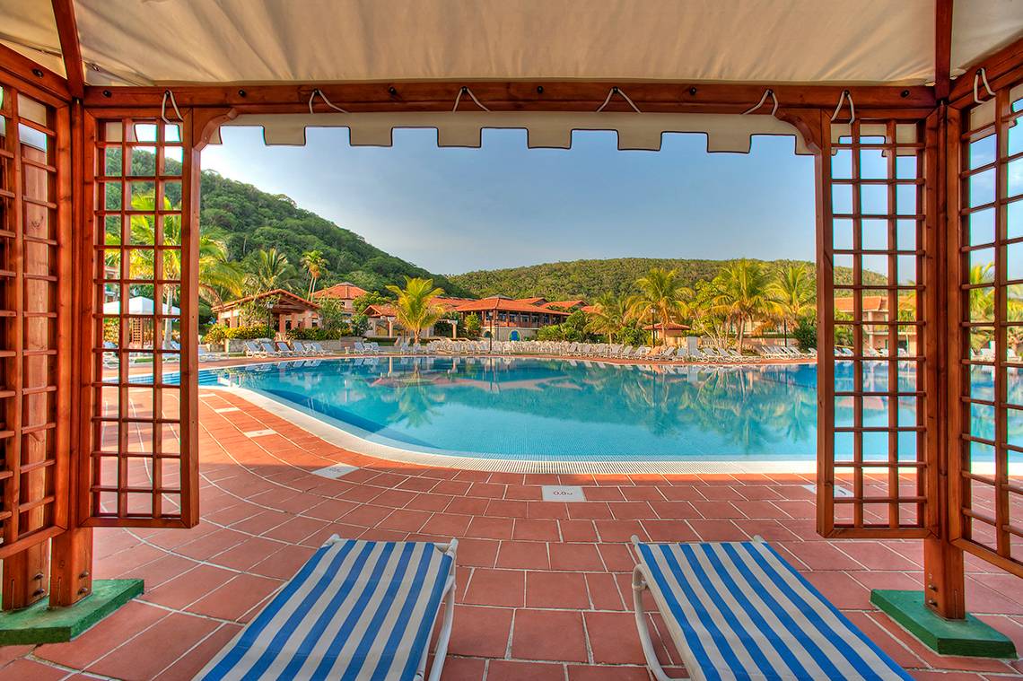 Außenpoolbereich des Memories Jibacoa Resorts mit Loungestühlen und Bergpanorama