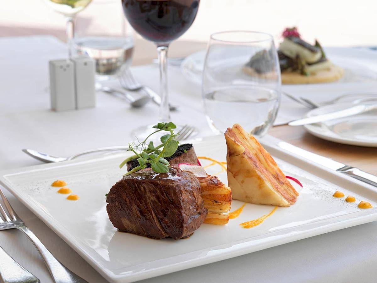 Ein Essen am Tisch des H10 Blue Mar Boutique Hotels mit Steak, Beilagen und Getränken.