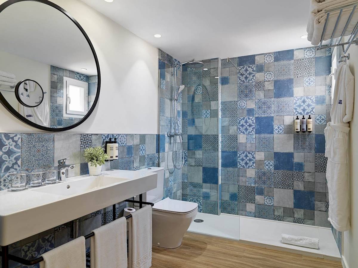 Das Badezimmer des H10 Casa del Mar Hotels mit blauen und grauen Fliesen, einem Spiegel, einem Waschbecken, einer Toilette und einer Dusche.