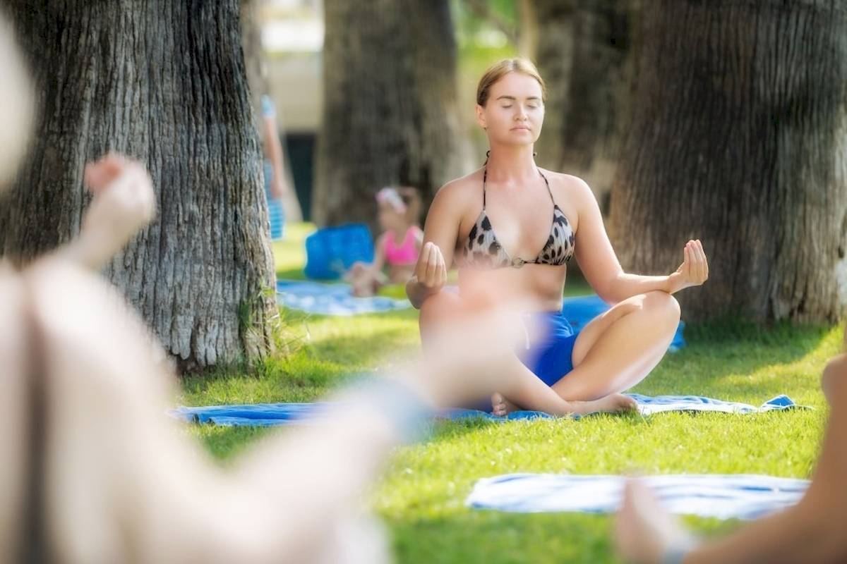 Frau im Bikini macht Yoga im Garten, mit anderen Personen im Hintergrund.