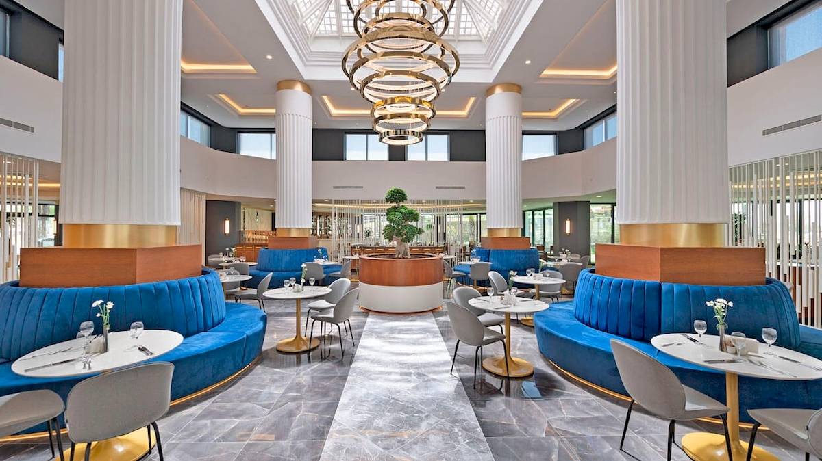 Ein elegantes Restaurant im Monachus Family Resort Sorgun mit blauen Sitzbänken und goldenen Tischen.