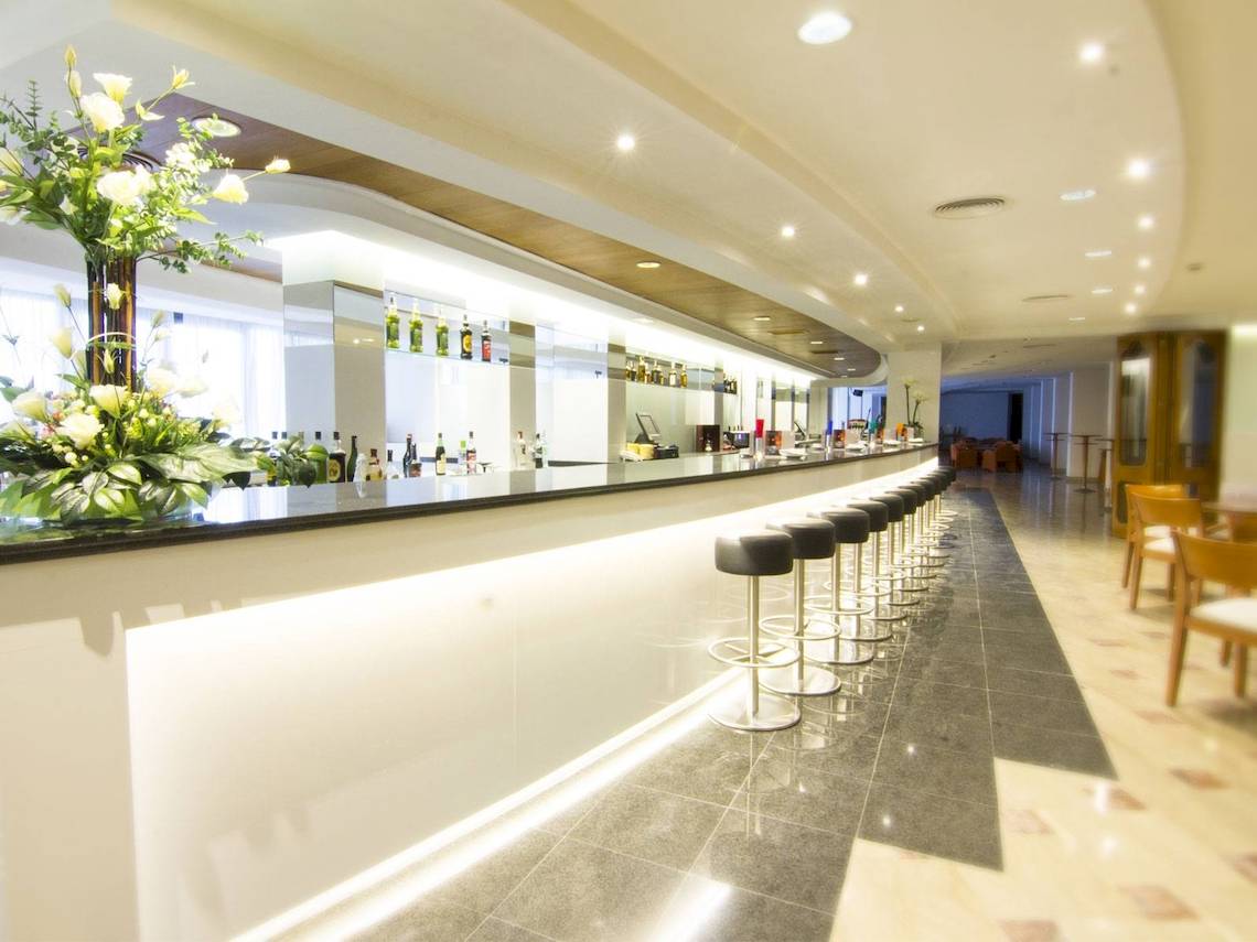 Bar im CM Castell de Mar Hotel mit weißen Stühlen und einer grünen Pflanze.