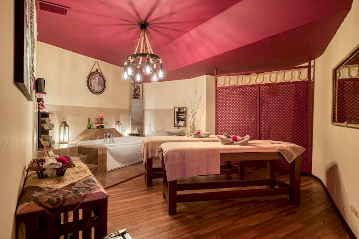 Spa-Zimmer im Seven Seas Hotel Life mit zwei Massagetischen, Badewanne und roten Decken.