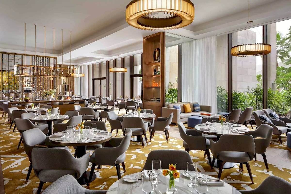 Innenansicht des Restaurants im Atlantis The Royal Hotel mit eleganten Tischen, Stühlen und goldenen Kronleuchtern.