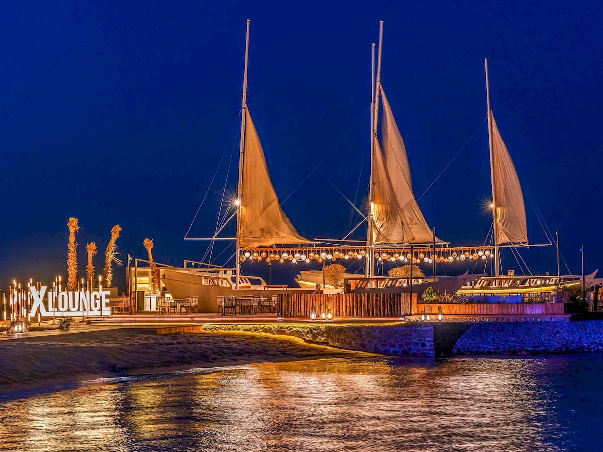 Nachtansicht des Rixos Premium Magawish Suites & Villas mit beleuchteten Segeln und Loungebereich am Wasser.