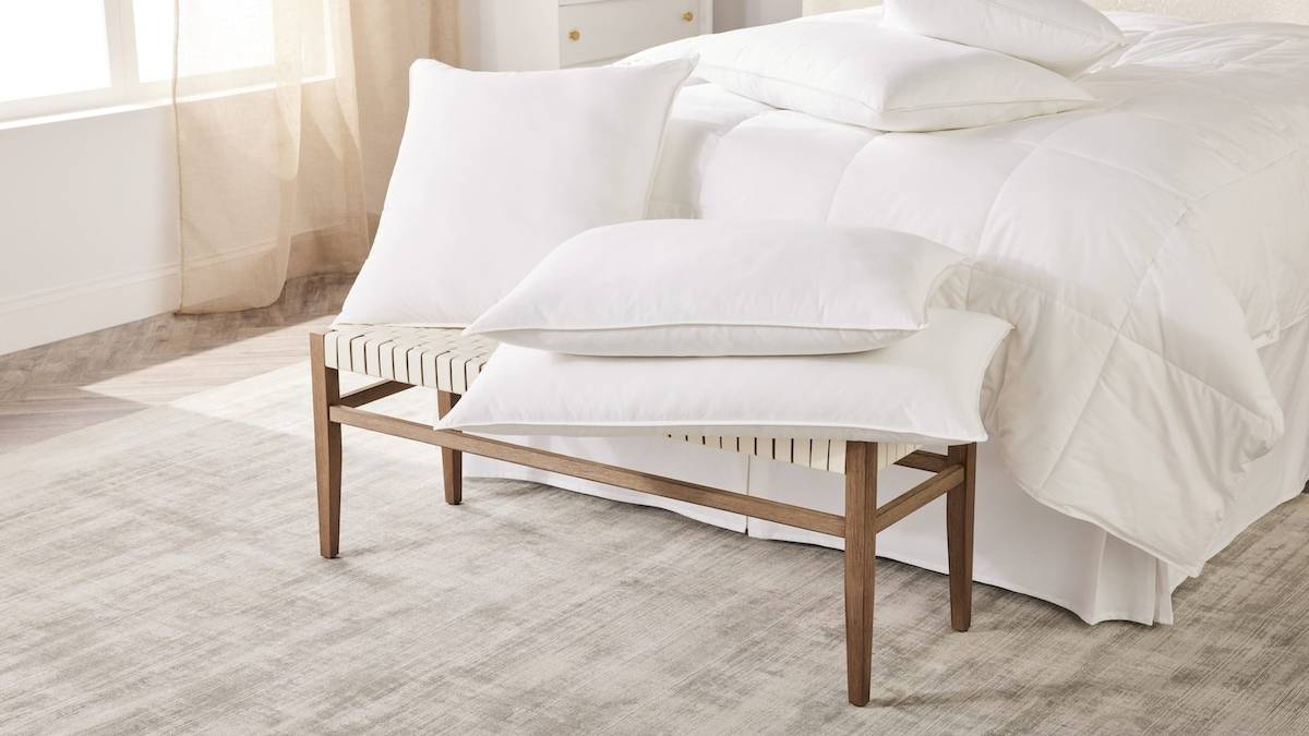 Ein Bett mit weißen Kissen auf einem Bankfussende im Mandarin Oriental, Costa Navarino.