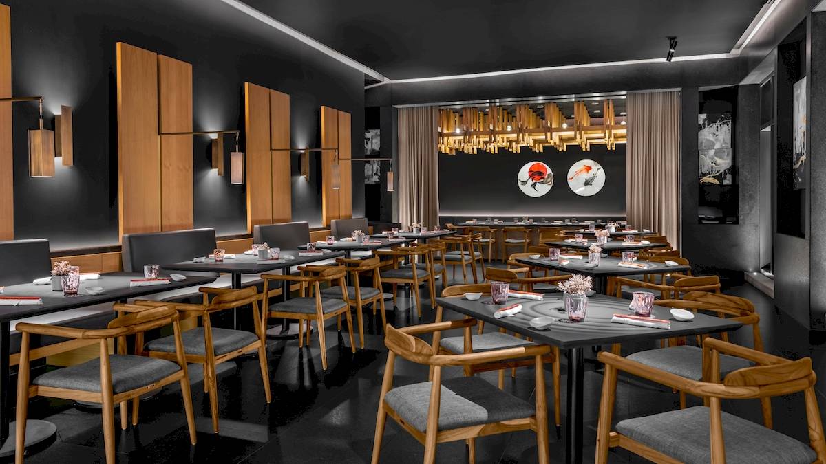 Innenansicht des Restaurants im Hilton Tulum Riviera Maya All-Inclusive Resort mit dunklen Wänden, Holztischen und Stühlen.