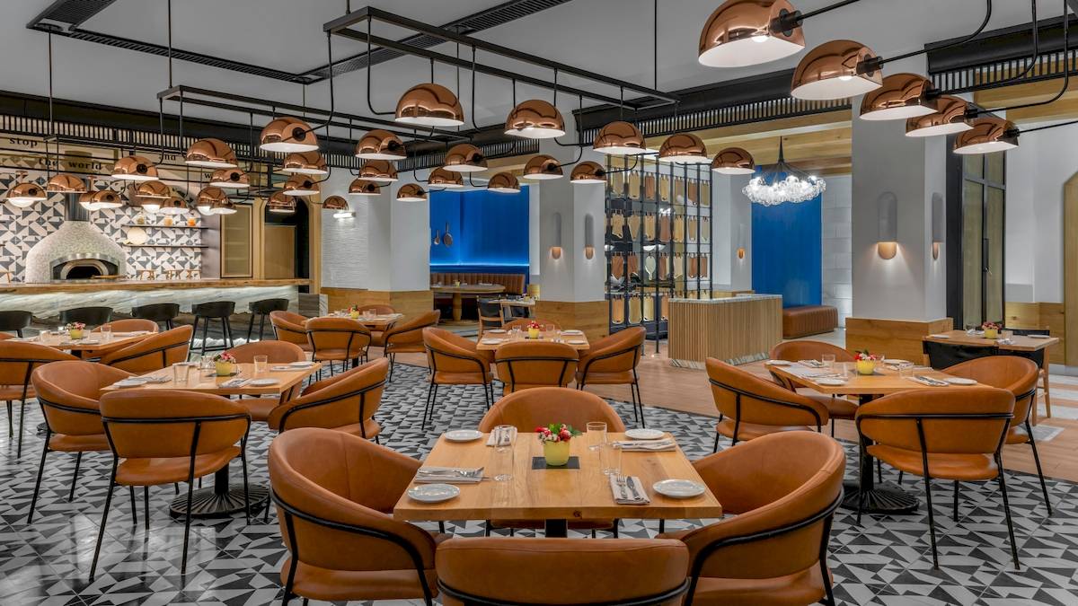 Innenansicht des Restaurants im Hilton Tulum Riviera Maya All-Inclusive Resort mit orangefarbenen Stühlen und Kupferlampen.