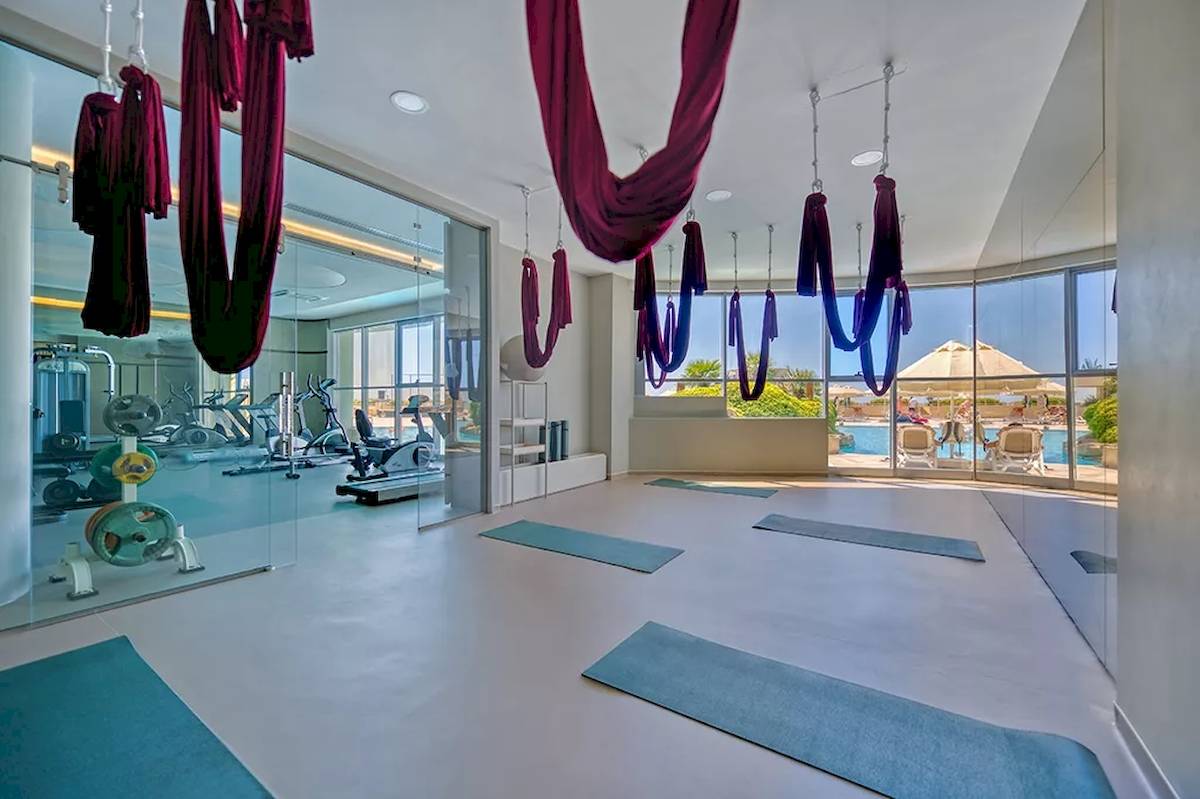 Yogaraum im Melas Resort mit Blick auf den Pool und Fitnessgeräten.