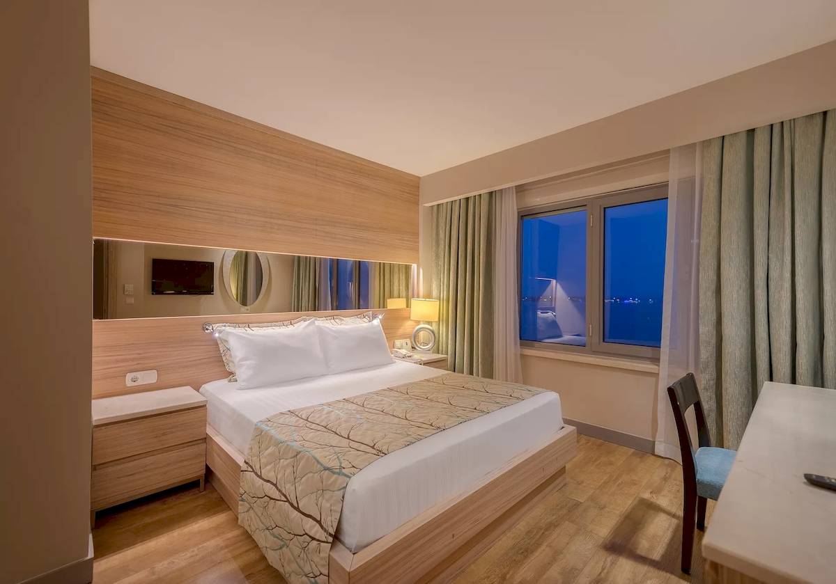 Innenansicht eines Hotelzimmers im Melas Resort mit einem Bett, Nachttisch, Spiegel und Fenster.