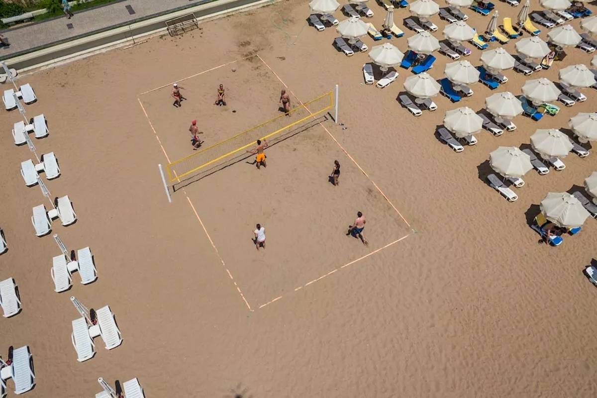 Besuch des Melas Resorts, Leute spielen Volleyball am Strand vor vielen Sonnenliegen