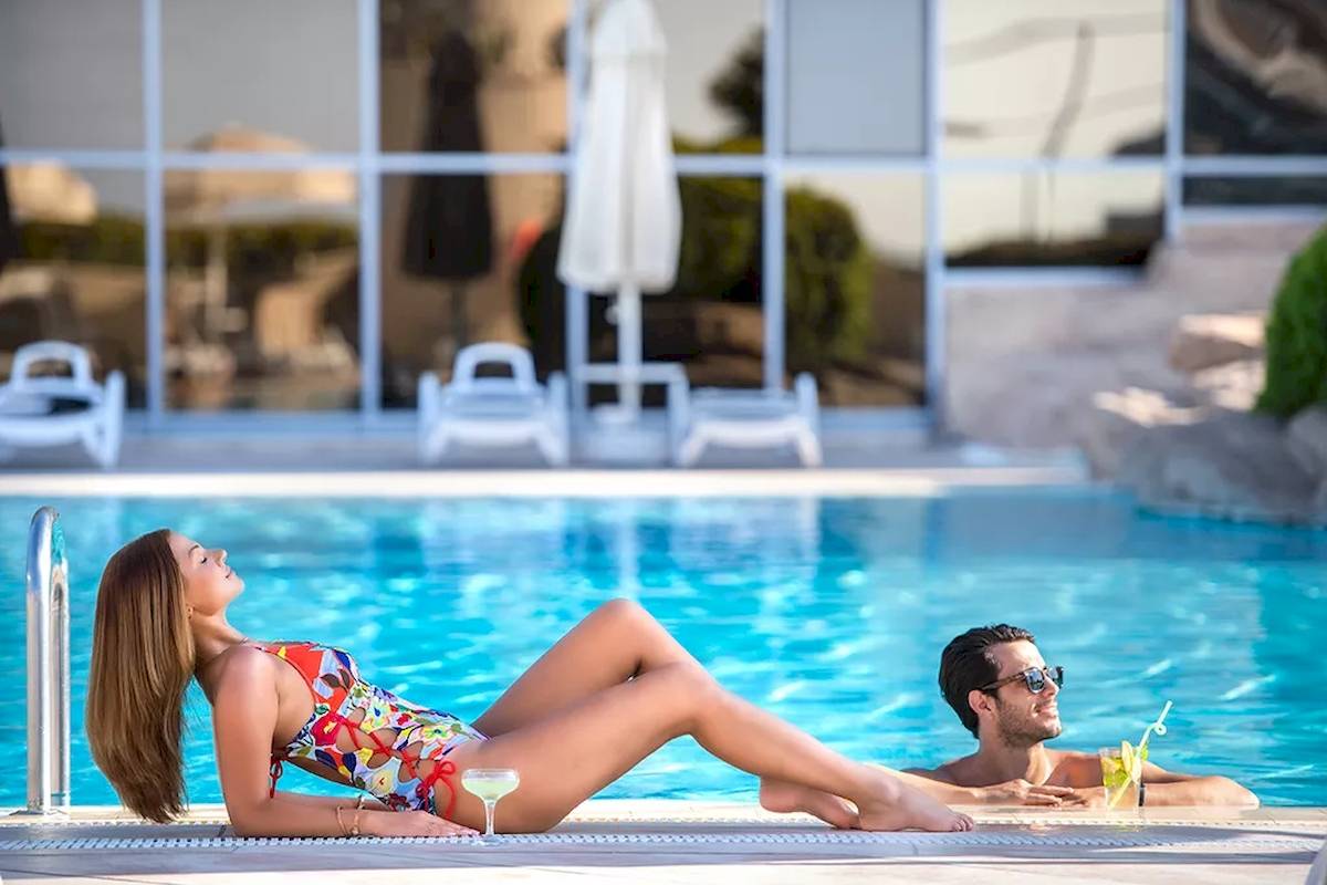 Ein Paar am Pool im Melas Resort, mit der Frau schwimmend und der Mann lachend.