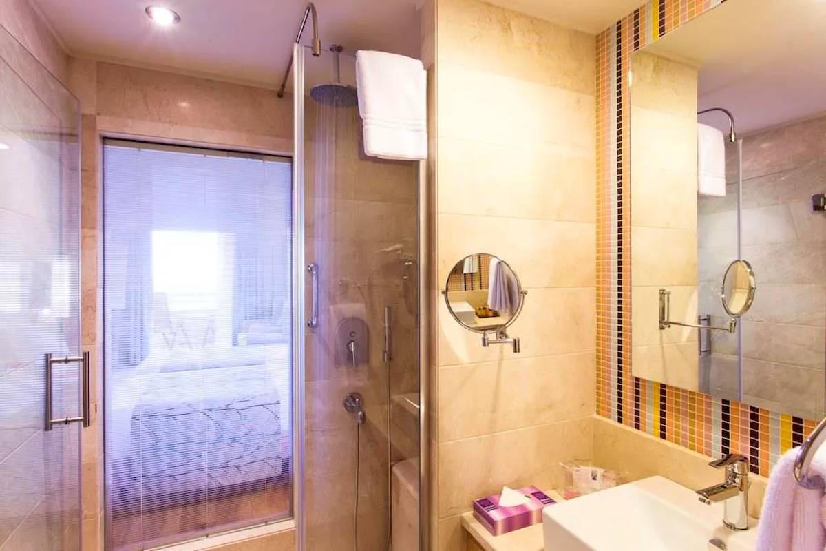 Badezimmer im Melas Resort mit einer Glasdusche, Handtüchern und einem Badezimmerspiegel.