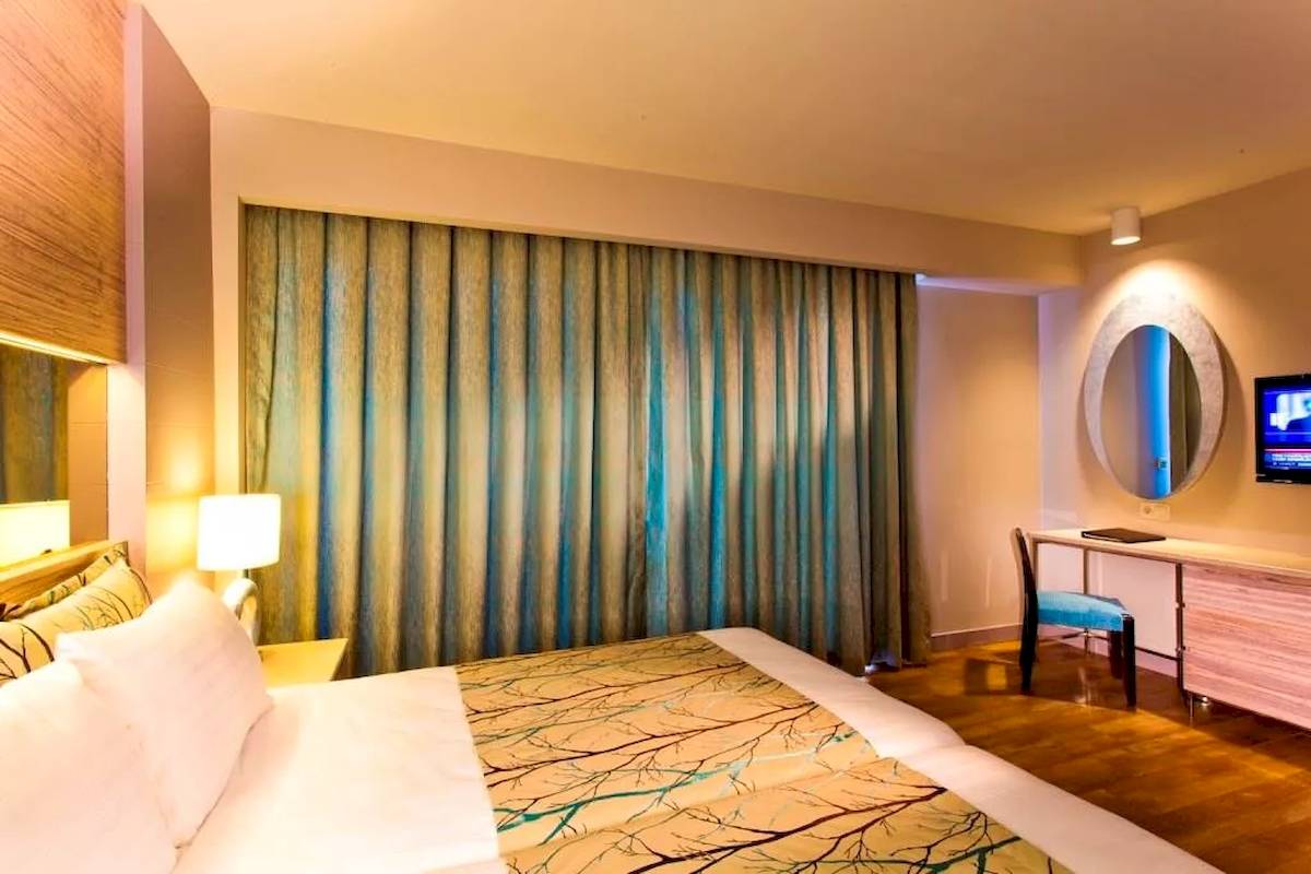 Innenansicht eines Hotelzimmers im Melas Resort mit Bett, Schreibtisch und Fernseher.