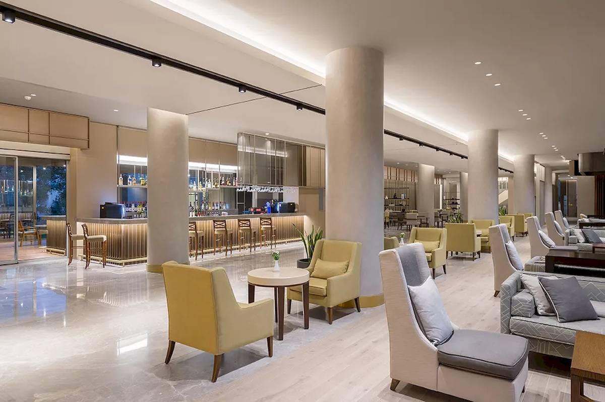 Lobby-Bereich des Melas Resorts mit Sitzbereichen, Bar und hoher Decke.