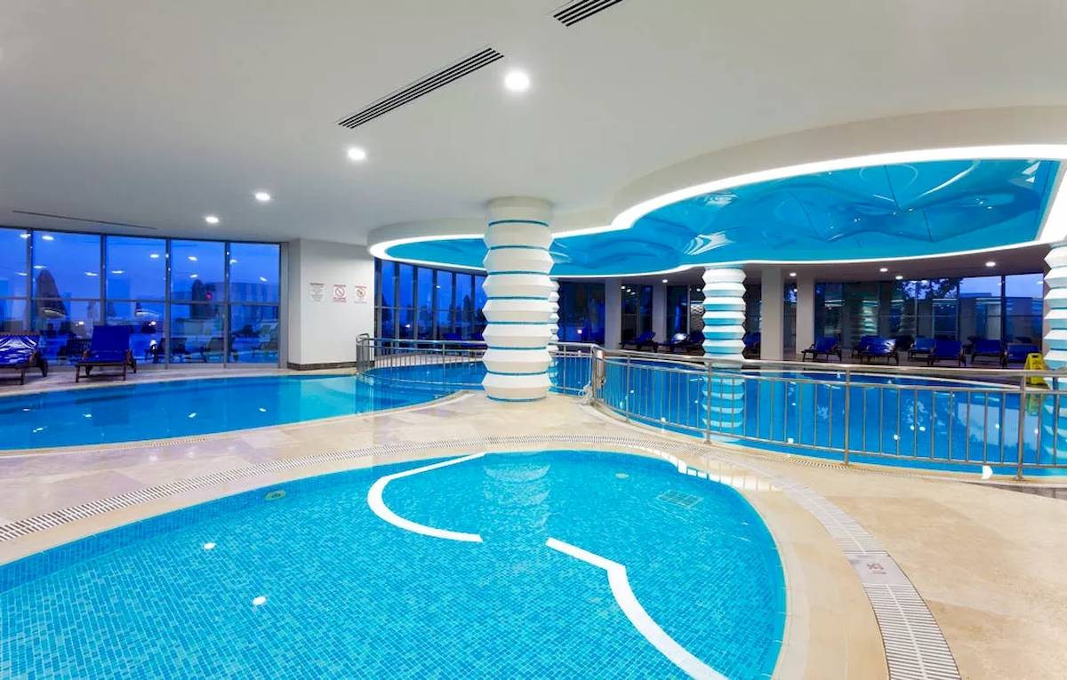 Innenpoolbereich des Melas Resorts mit blauen Wänden und Säulen, gefüllt mit klarem Wasser.