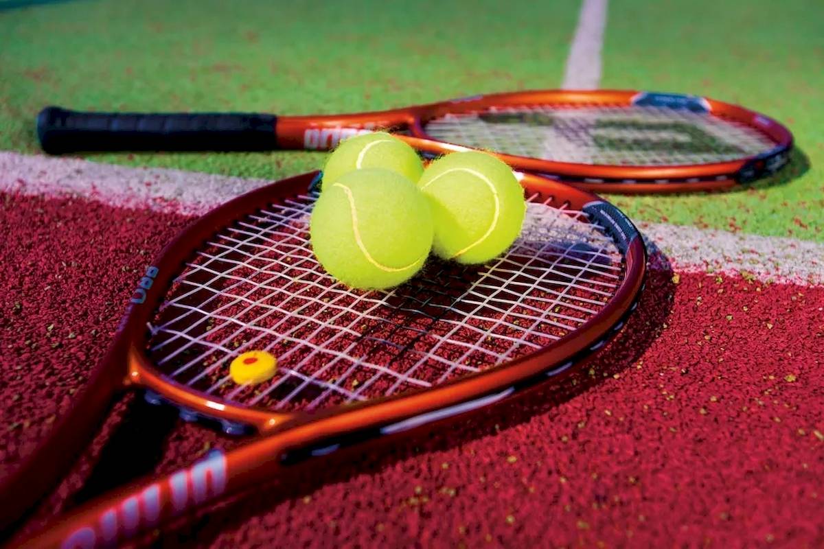 Zwei rote Tennisschläger und drei gelbe Tennisbälle auf einem roten Tennisplatz