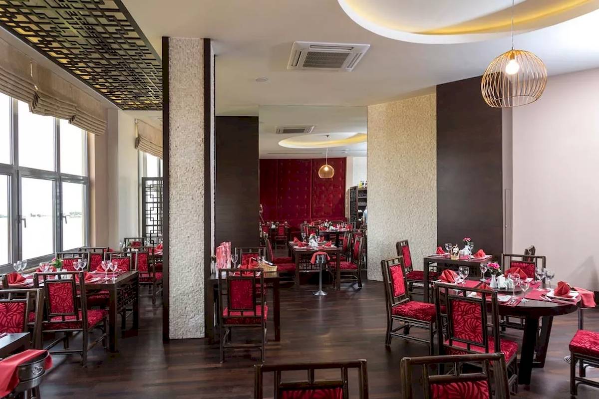 Innenansicht des Restaurants im Melas Resort mit roten Stühlen und Tischen, dekorativ beleuchtet.