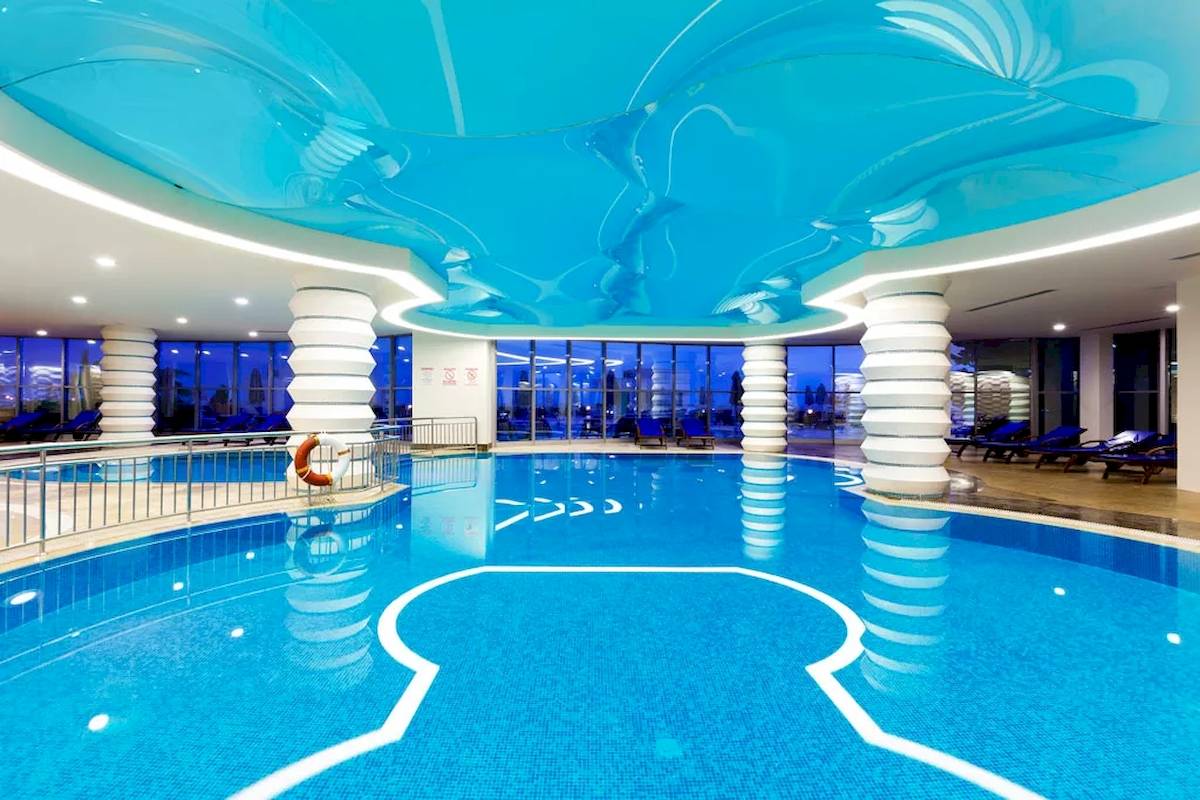 Innenansicht des Schwimmbeckens im Melas Resort, mit blauer Decke und weißen Säulen.