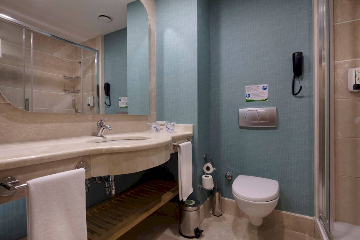Badezimmer des Novum Garden Side Hotel mit Waschbecken, Spiegel und Toilette.