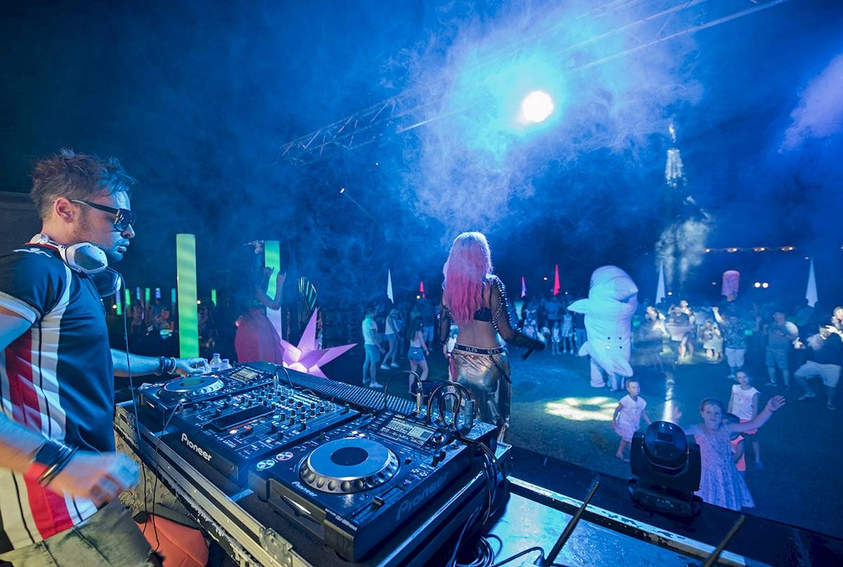 DJ auf der Bühne im Novum Garden Side Hotel bei einer Nachtveranstaltung mit vielen Gästen.