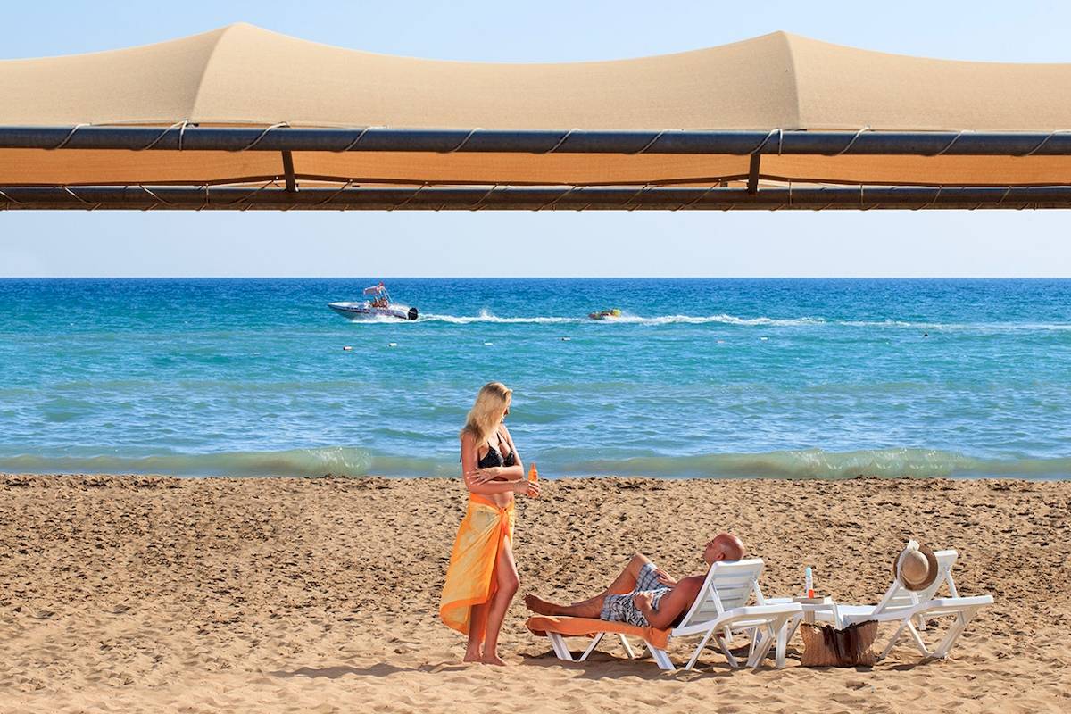 Strandszene mit Novum Garden Side Hotel, Frau in Bikini und Mann auf Sonnenliegen