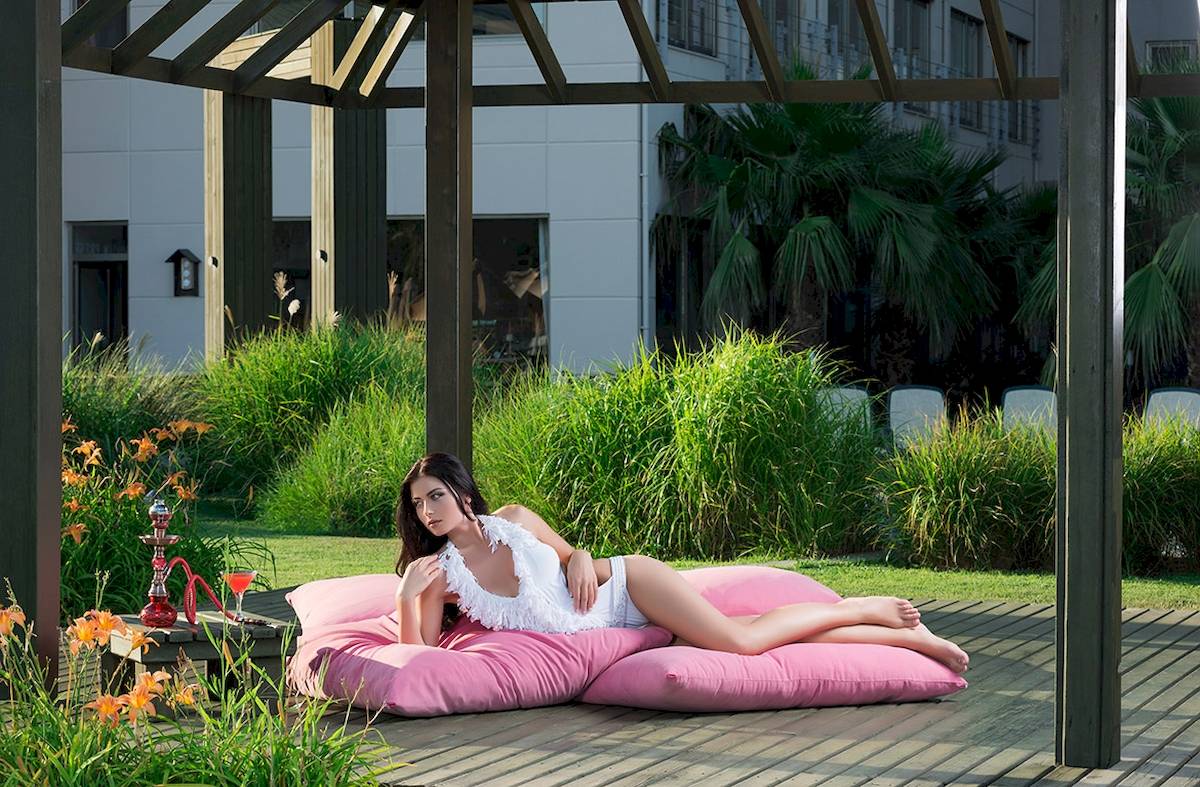 Frau im Garten des Novum Garden Side Hotels, im weißen Outfit auf einem rosa Kissen liegend.
