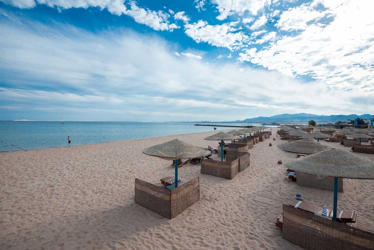 Strand mit Sonnenschirmen und Liegen im Freien, Blick auf das Meer und Berge.