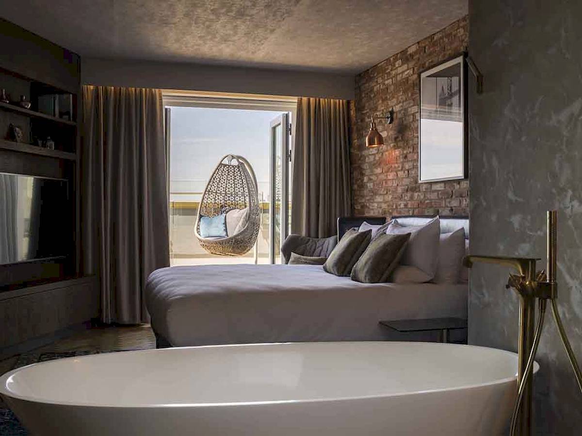 Innenansicht eines Zimmers im Novotel London Canary Wharf mit Bett, Badewanne, Hängesessel und Aussicht.