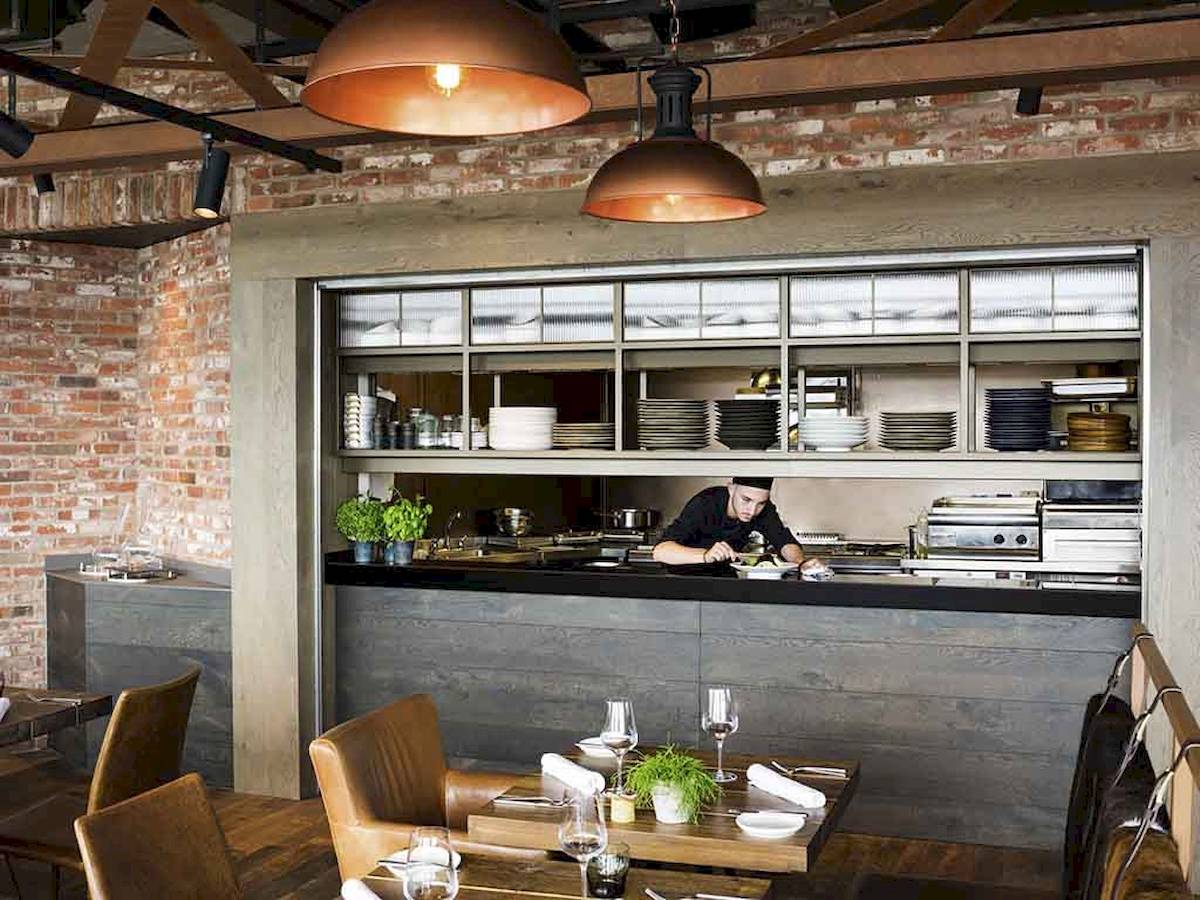 Innenansicht des Restaurants im Novotel London Canary Wharf mit Koch hinter der Theke und eingerichteten Tischen.