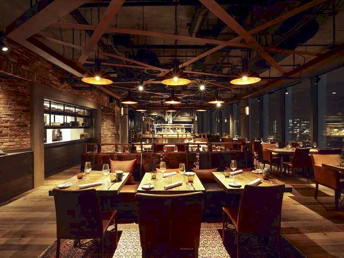 Innenansicht des Restaurants im Novotel London Canary Wharf mit Tischen und Stühlen, Beleuchtung und Holzboden.