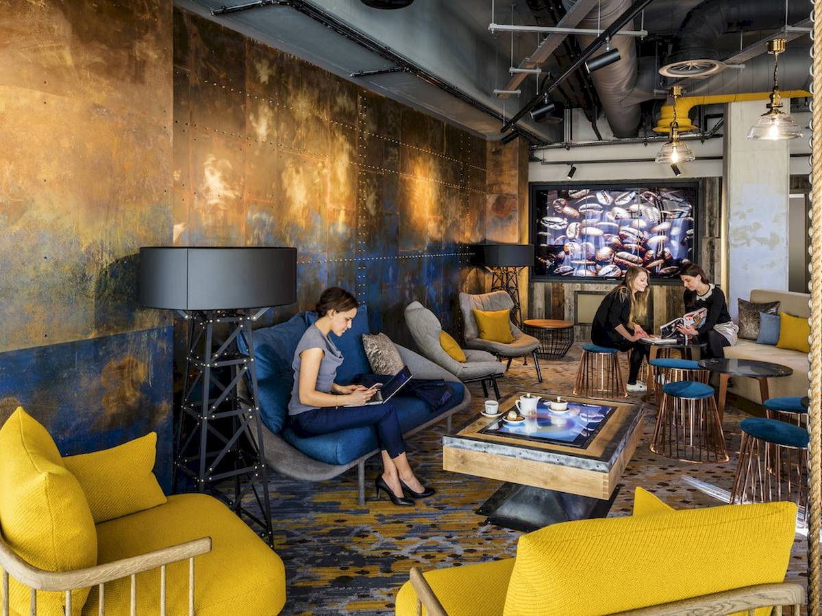 Loungebereich im Novotel London Canary Wharf Hotel mit Gäste, die an Tischen sitzen und arbeiten.