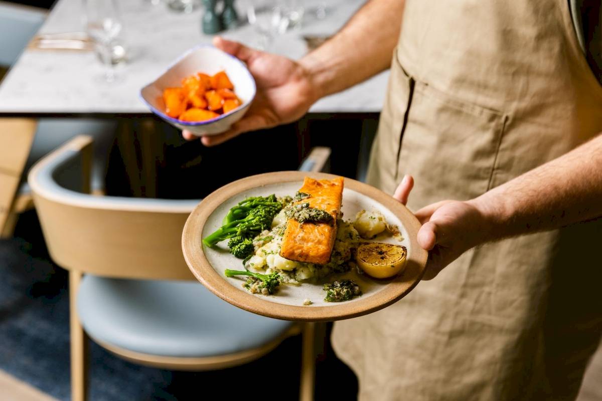 Mitarbeiter des Leonardo Hotel London Croydon serviert ein Gericht mit Lachs, Broccoli und Kartoffelpüree.