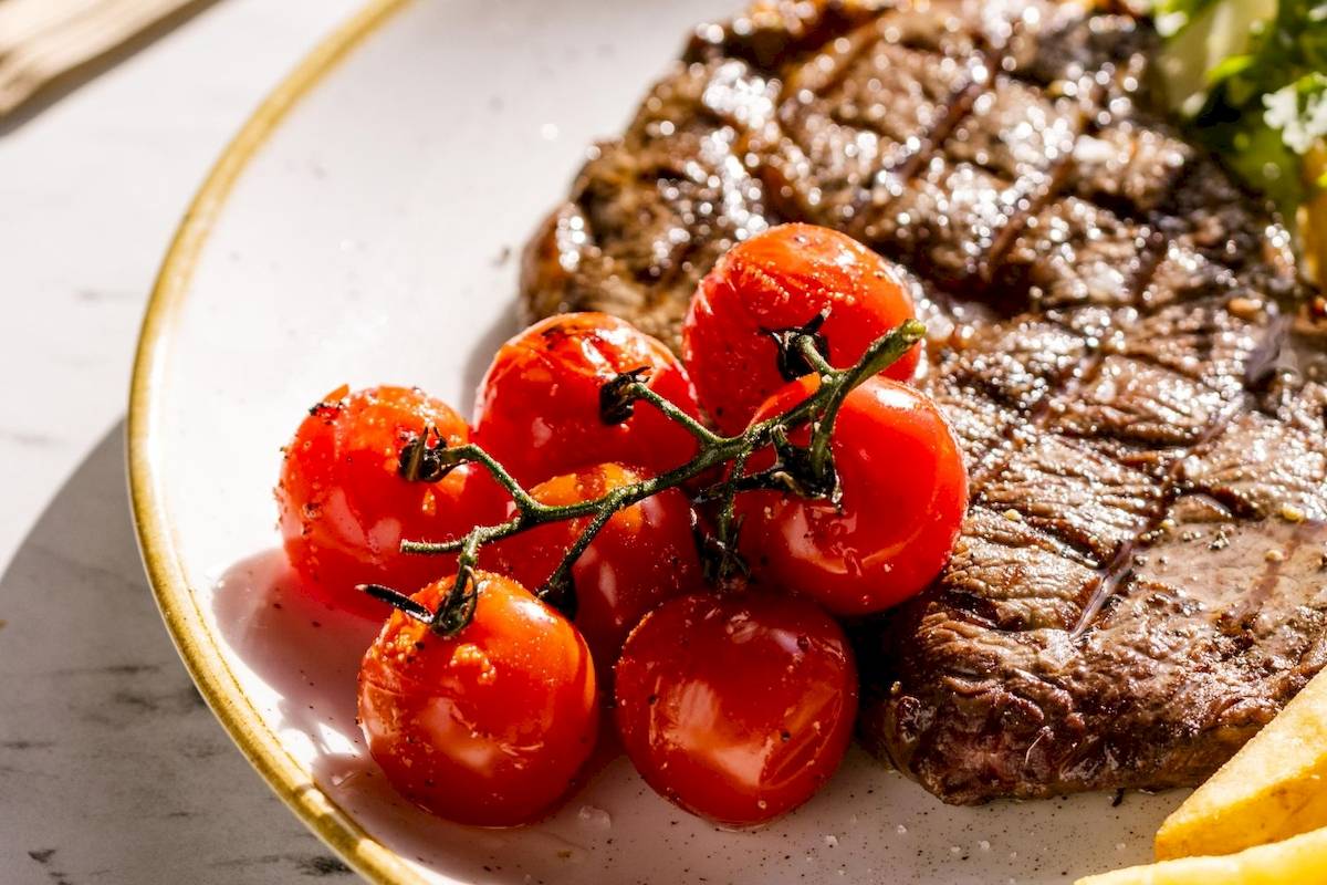 Gegrilltes Steak mit Tomaten und Pommes auf einem weißen Teller.