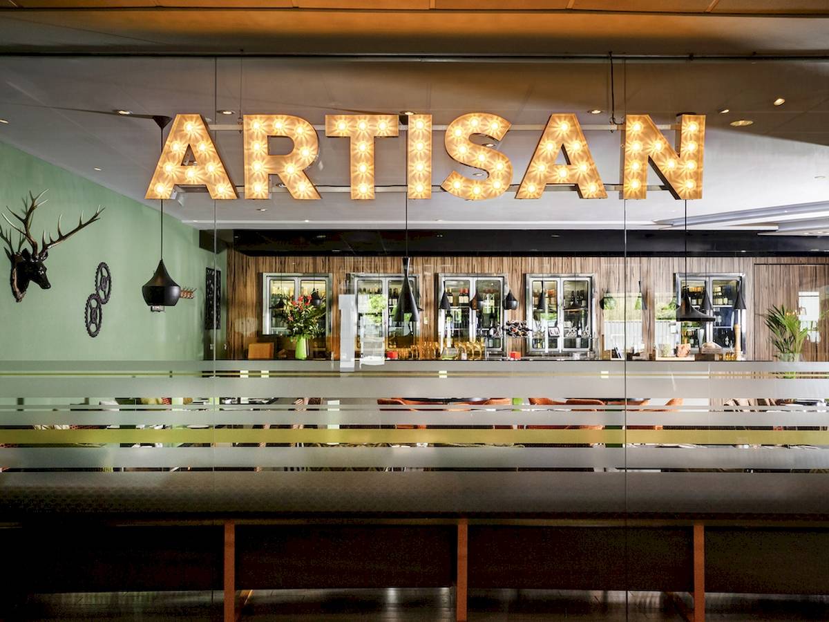 Innenansicht der Artisan Bar im Novotel London West mit großem Leuchtschriftzug und Holzelementen.