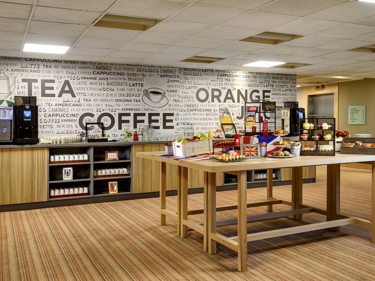 Barbereich im Novotel London West Hotel mit einer Wand voller Kaffeenamen und einer Theke mit verschiedenen Getränken und Speisen.