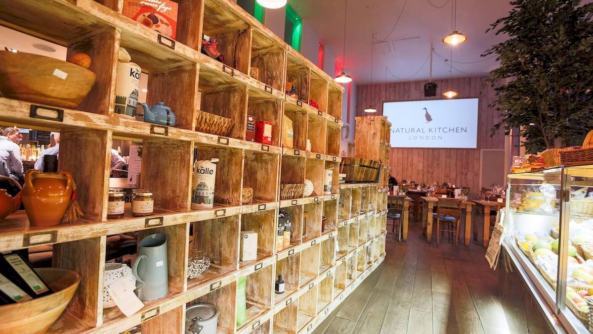 Innenansicht des Natural Kitchen London im DoubleTree by Hilton Tower of London mit Regalen, Tischen und einer Tafel
