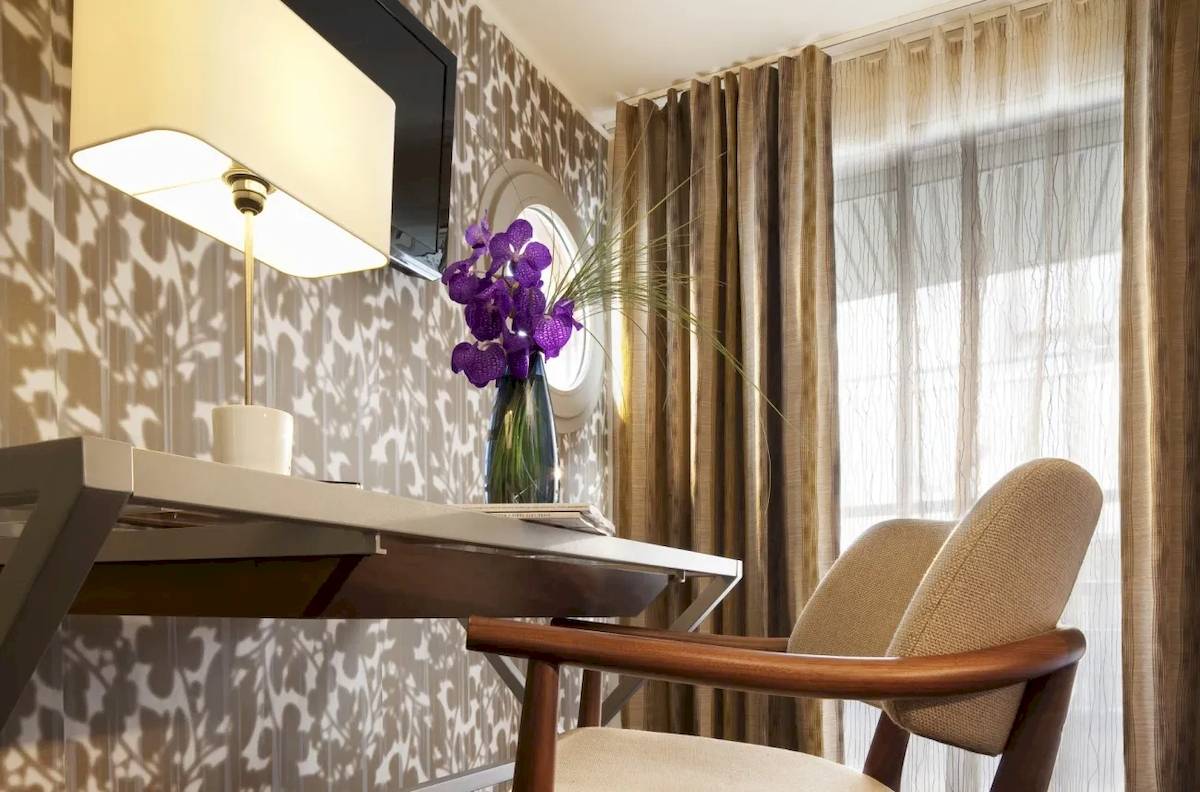 Schreibtisch im Hotelzimmer Les Jardins d' Eiffel mit einer Lampe, Blumenvase und einem Fenster.