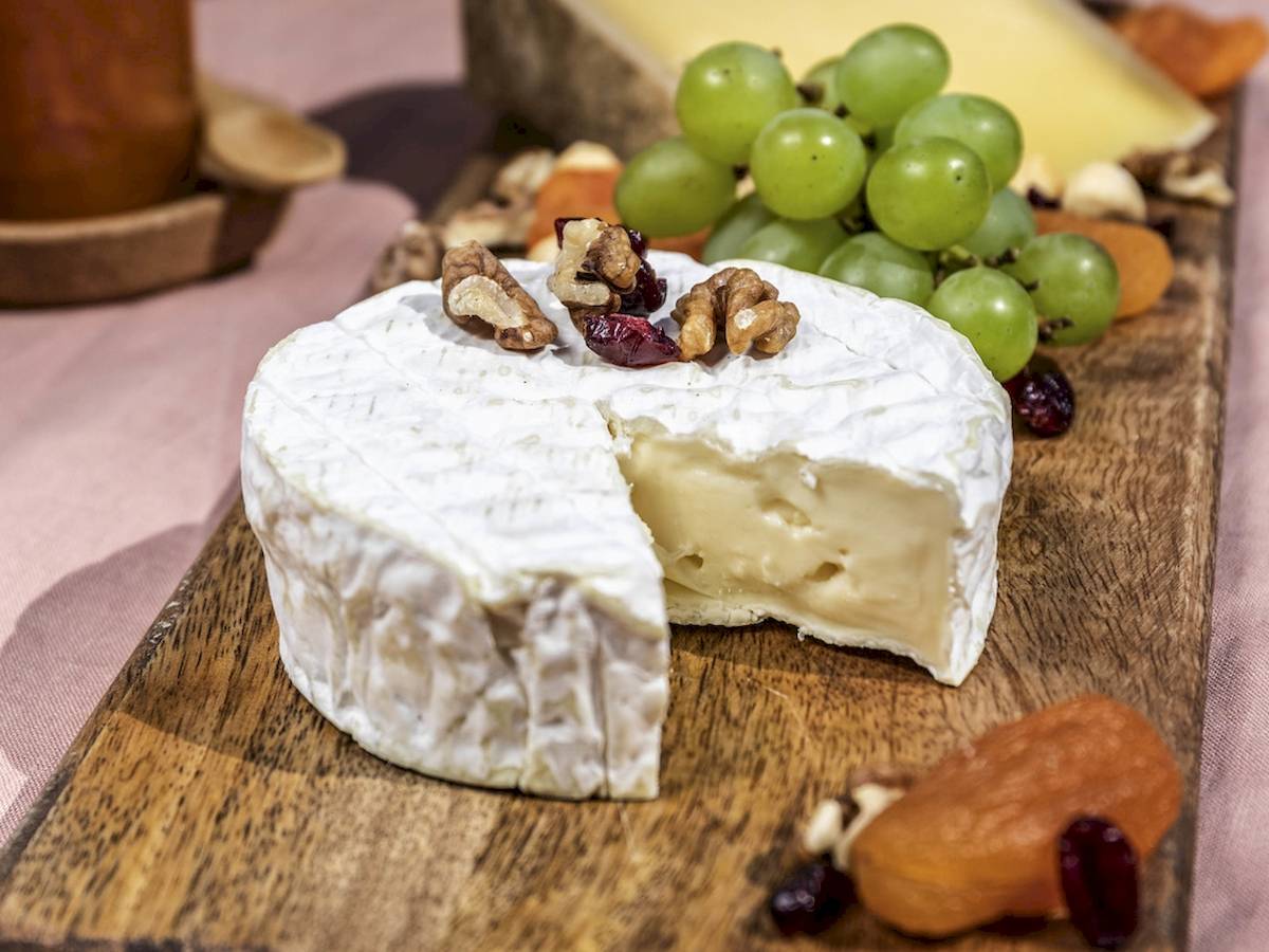 Eine Schnitte von weißem Käse mit Nüssen und Obst auf einem Holzbrett.