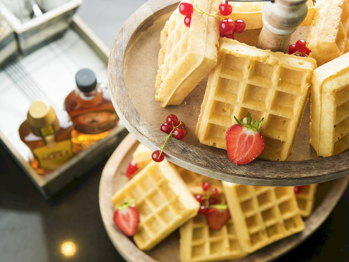 Gebackene Waffeln mit roten Beeren und Honig auf einem Tablett im Novotel Paris Tour Eiffel