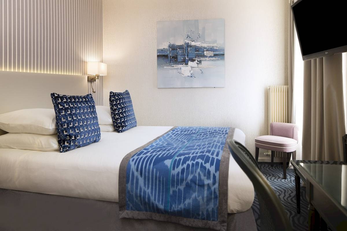 Ein geschmackvoll eingerichtetes Zimmer im Victor Hugo Paris Kléber Hotel mit einem Doppelbett, Kissen und einem Gemälde an der Wand.