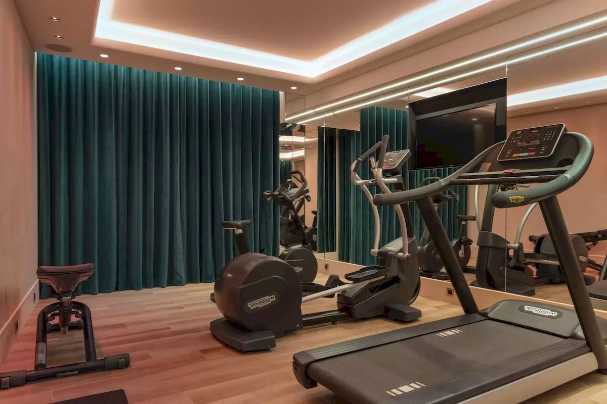 Fitnessraum im Victor Hugo Paris Kléber Hotel mit Laufband, Rudergerät und blauen Vorhängen.