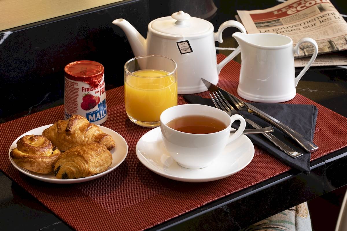 Frühstück im Hotel Victor Hugo Paris Kléber mit Croissants, Tee, Orangensaft und Zeitung.