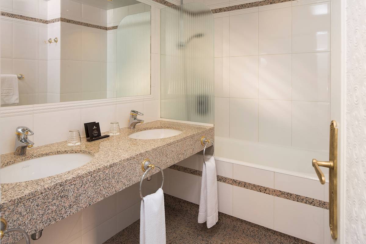 Badezimmer im Victor Hugo Paris Kléber Hotel mit weißen Fliesen, Marmorwaschtisch und Badewanne.
